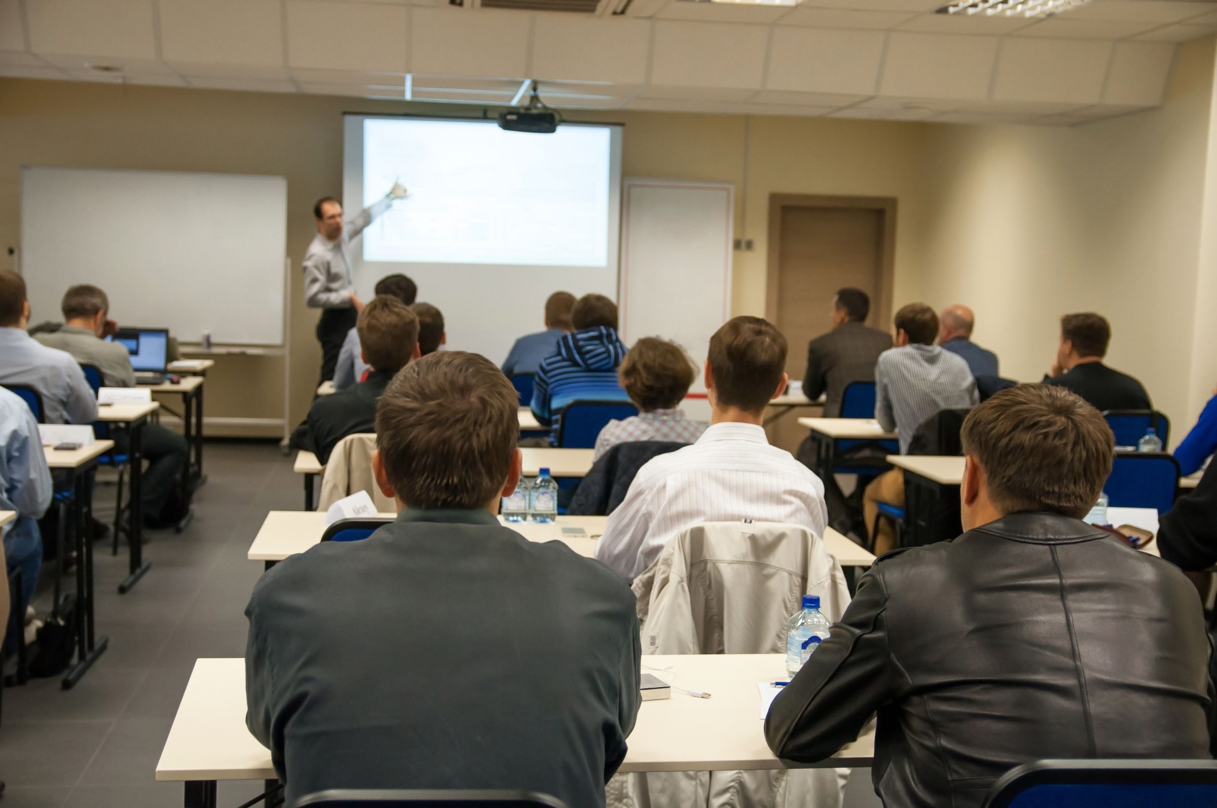 A presenter at a projector screen, with a full room of attendees